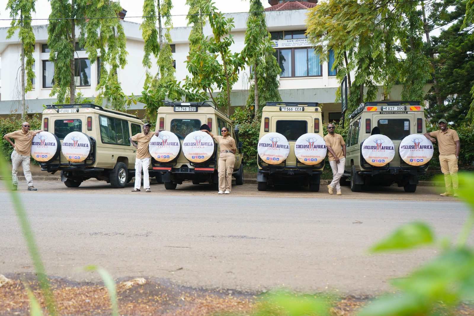 Five Enclose Africa Safaris guides standing with four branded Land Cruisers outside the company office in Arusha, Tanzania